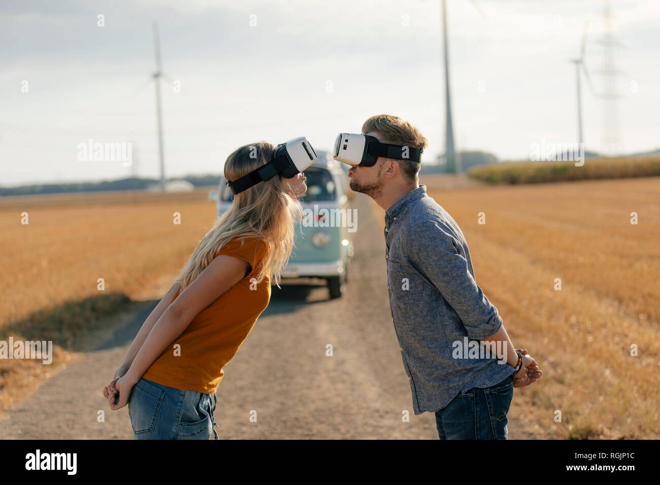 Jeune couple portant des lunettes VR s'embrasser au camping-van in rural landscape Banque D'Images