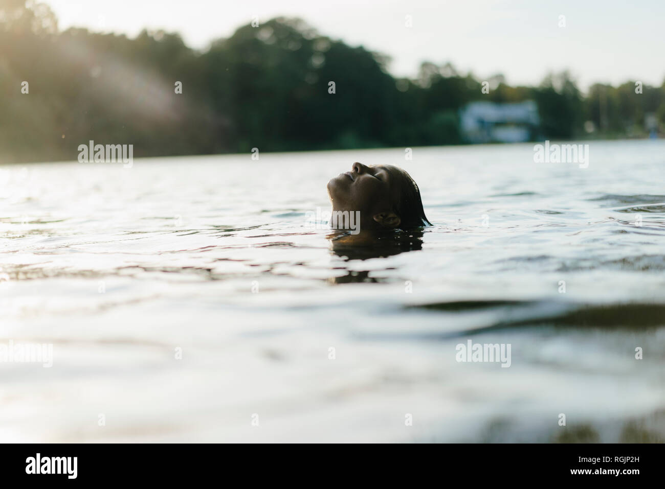 Femme flottant dans un lac au coucher du soleil Banque D'Images