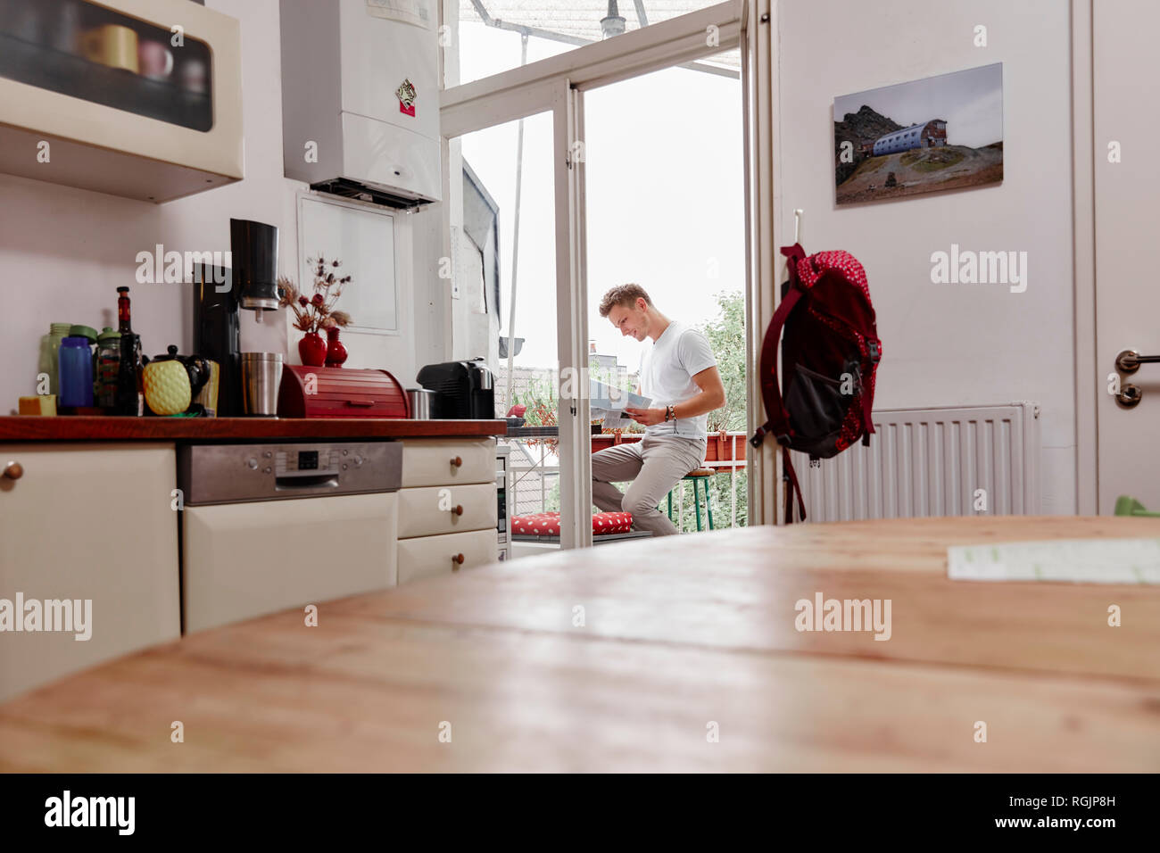 Jeune homme assis sur le balcon à la maison lire la carte Banque D'Images