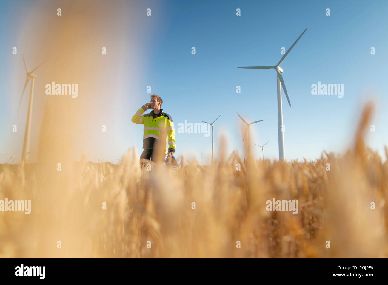 Permanent ingénieur dans un champ à une ferme éolienne talking on cell phone Banque D'Images