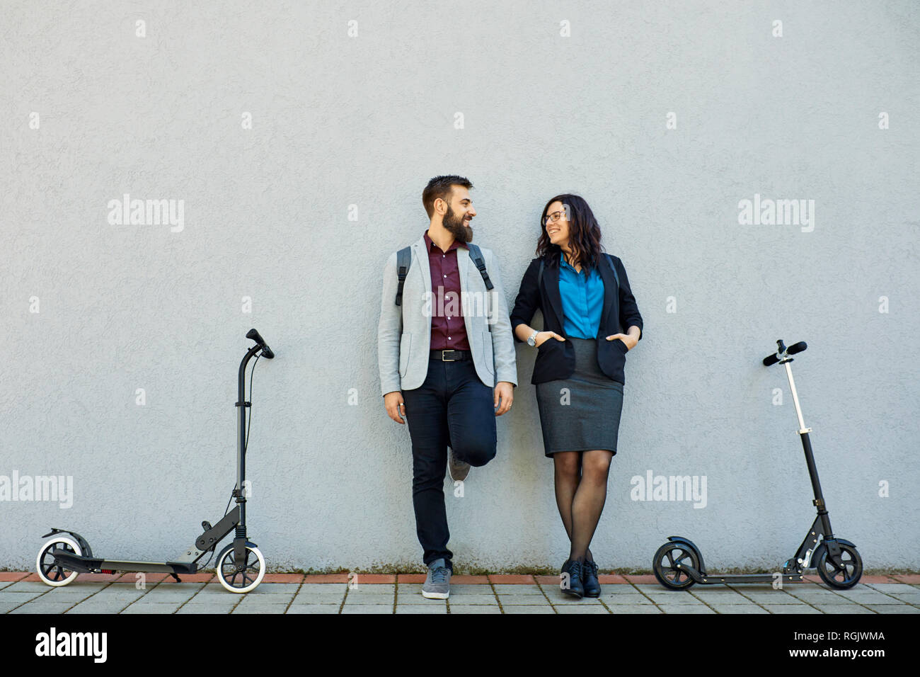 Smiling businessman and businesswoman avec scooters appuyé contre un mur Banque D'Images