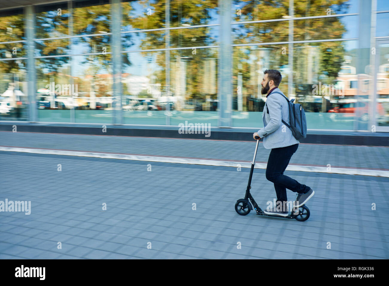 Businessman riding scooter le long office building Banque D'Images