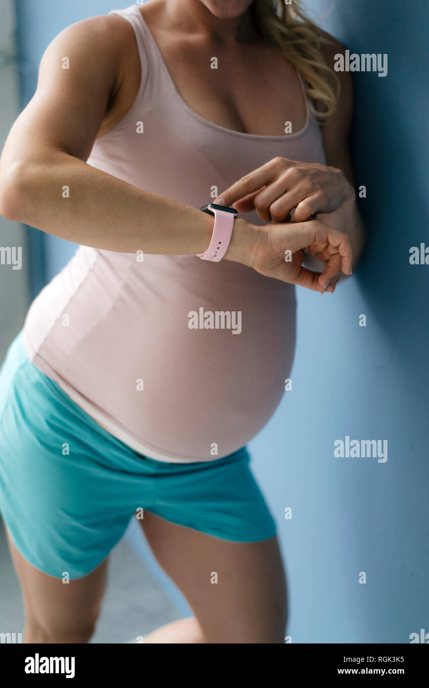 La mi-section of pregnant woman looking at smartwatch mur bleu Banque D'Images