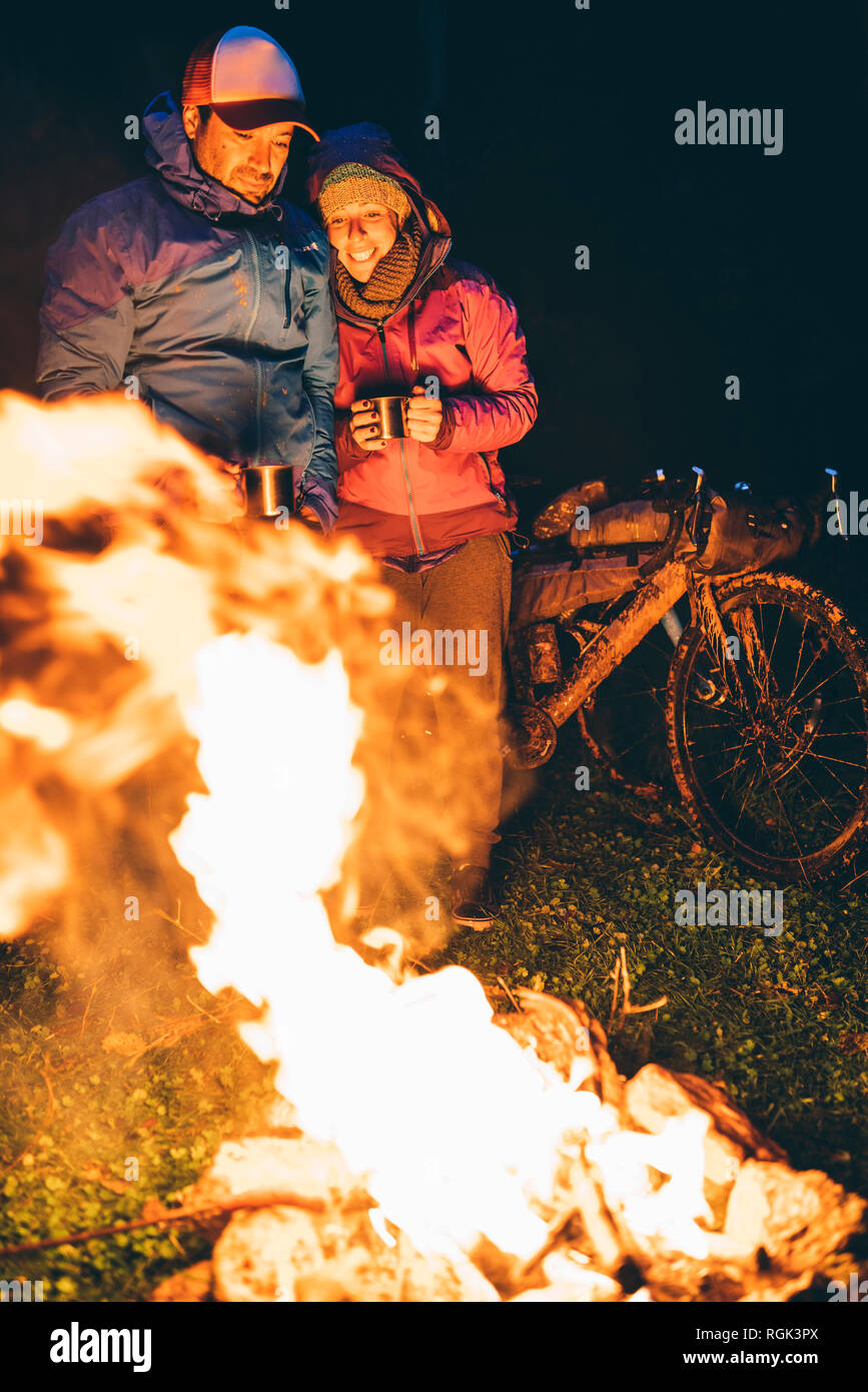 Couple avec avec des vélos debout à un feu de camp à la flamme à Par nuit Banque D'Images