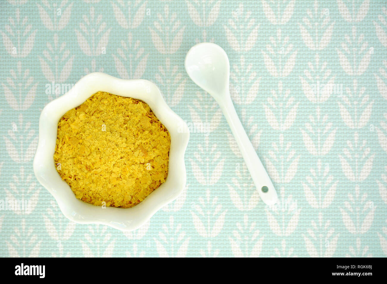 La levure alimentaire en flocons blanc cannelé bol et cuillère sur fond texturé turquoise pâle tourné à partir de ci-dessus. Format horizontal avec place pour le texte. Banque D'Images