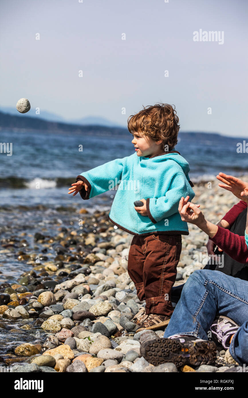 Bébé garçon sur un rivage rocailleux de lancer des pierres dans l'eau. Banque D'Images