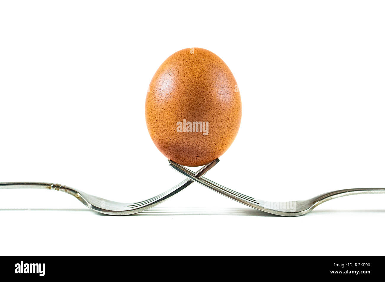 Un d'œufs biologiques brun en équilibre sur deux fourches isolé sur un fond blanc. Banque D'Images