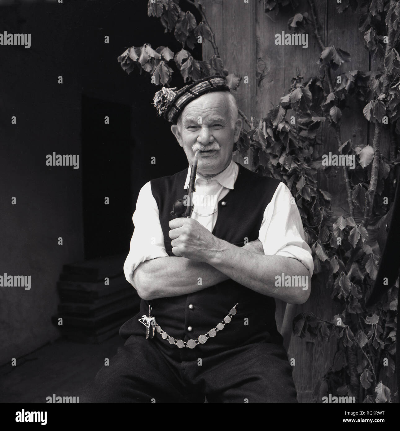 Années 1950, historique, portrait d'un vieil homme en costume national allemand assis à l'extérieur fumer une longpipe bavarois traditionnel, Bavière, Allemagne Banque D'Images