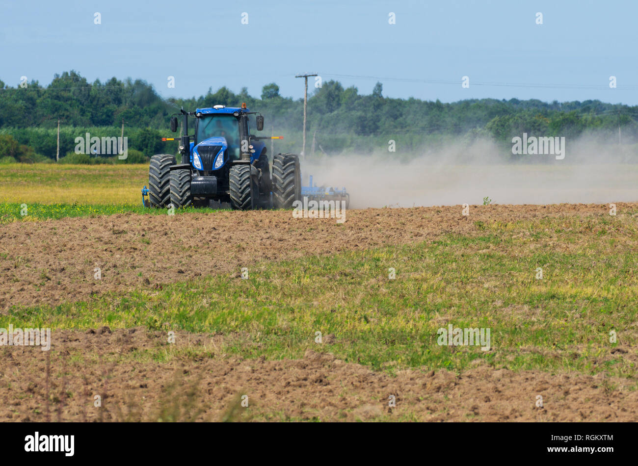 Vue avant du tracteur laboure le terrain avec une herse de fer dans la saison de labour avec la poussière tourbillonnante Banque D'Images