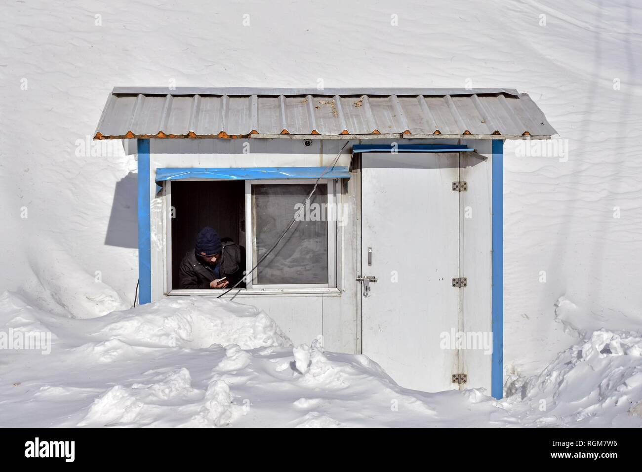 Un agent de la circulation vu contrôler son téléphone portable à l'intérieur d'un stand d'assistance du trafic sur une journée d'hiver ensoleillée dans Gagangir domaine de Ganderbal district, à environ 80 kms de Srinagar, Cachemire sous administration indienne. Le Cachemire est la région géographique la plus au nord du sous-continent indien. Il est en ce moment un territoire contesté, administré par trois pays : l'Inde, le Pakistan et la Chine. Banque D'Images
