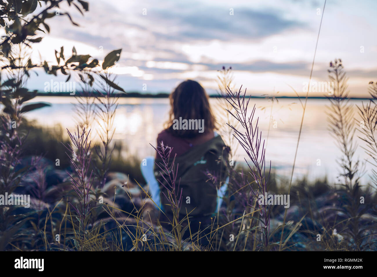 Jeune femme assise au bord du lac Inari, looking at view, Finlande Banque D'Images