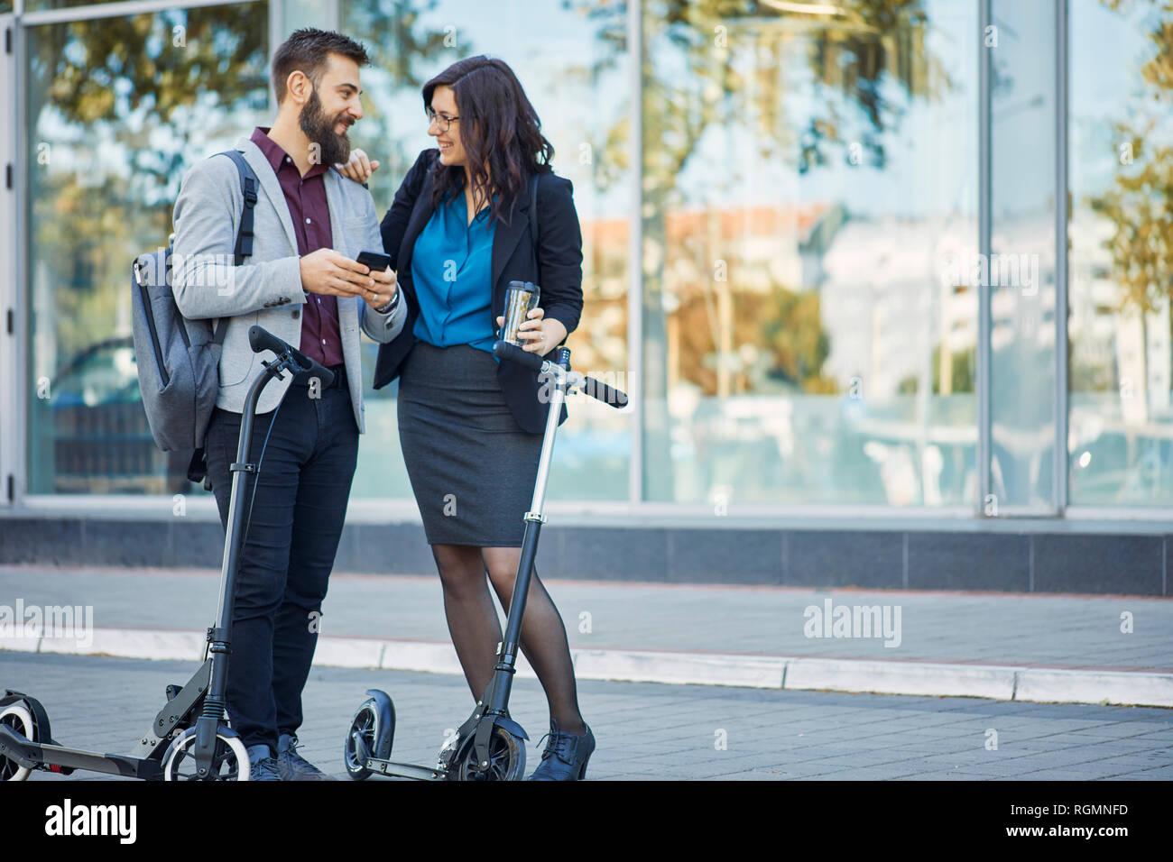 Smiling businessman and businesswoman talking on scooters avec pavement Banque D'Images