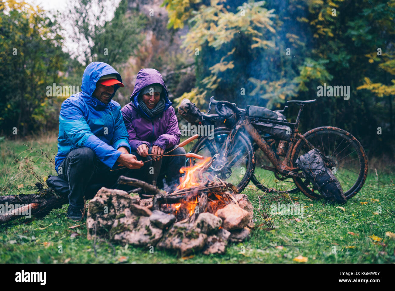 Laughing couple avec avec vélos bmx assis au feu de camp griller saucisses Banque D'Images