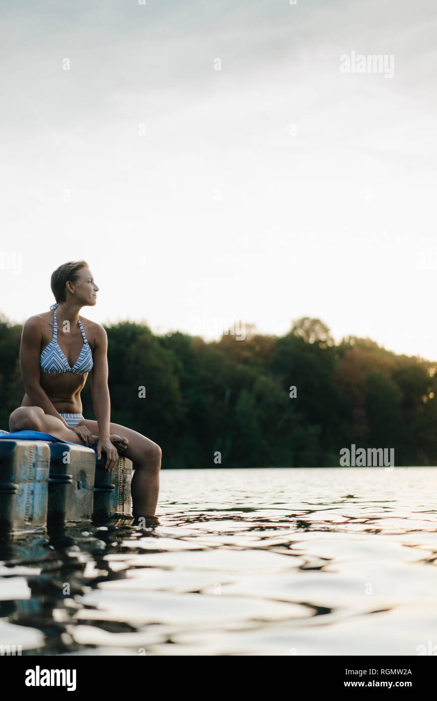 Femme portant un bikini assis sur un flotteur en un lac Banque D'Images