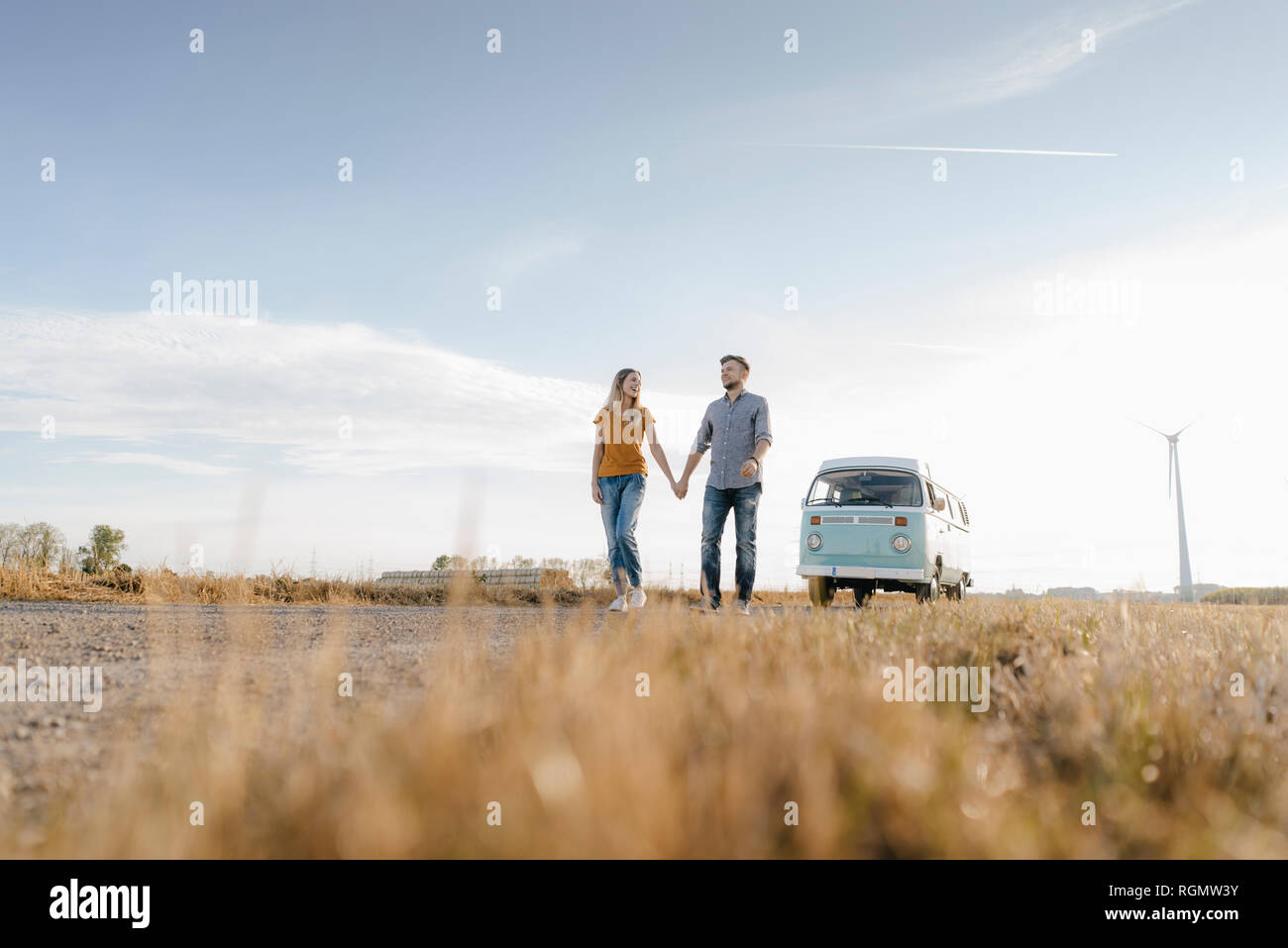 Jeune couple en train de marcher sur un chemin de terre à camper van in rural landscape Banque D'Images