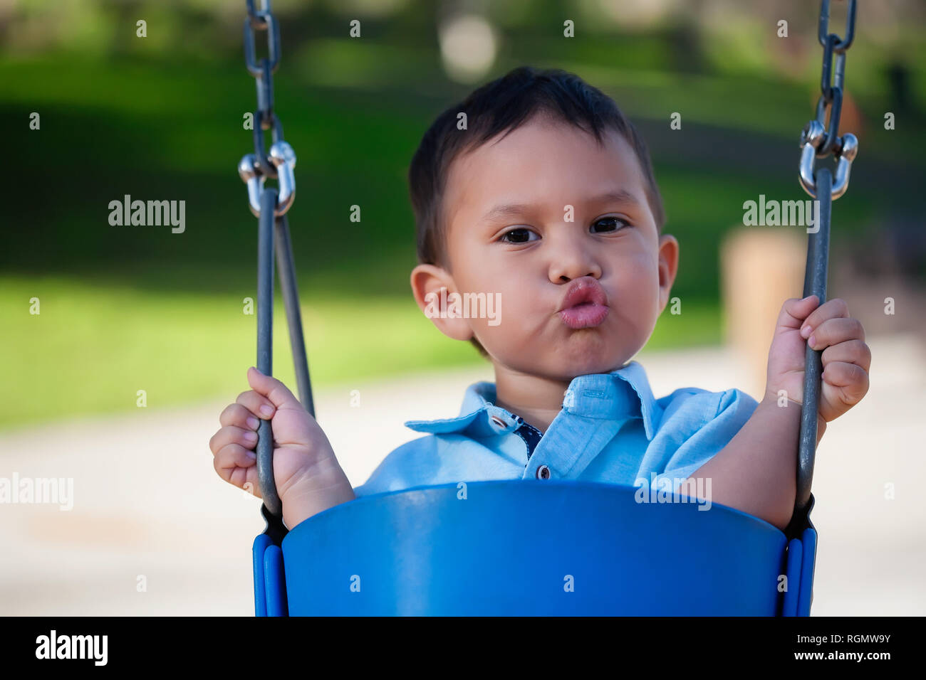 Cute little boy sitting et Holding on to a blue swing tout en soufflant des baisers avec les lèvres plissées. Banque D'Images