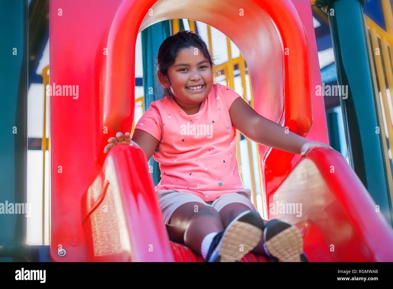 Une jolie jeune fille hispanique avec un sourire mignon a l'air détendu alors qu'elle s'apprête à glisser le long d'une aire de glisse. Banque D'Images