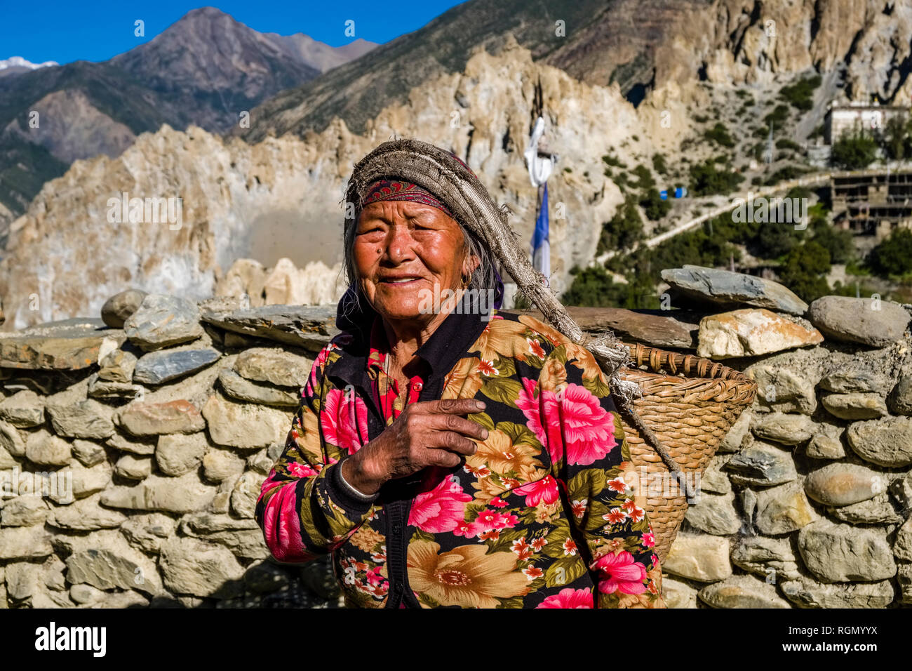Une femme porte un panier dans la vallée de l'Upper Marsyangdi, nuageux paysage alpin dans la distance Banque D'Images