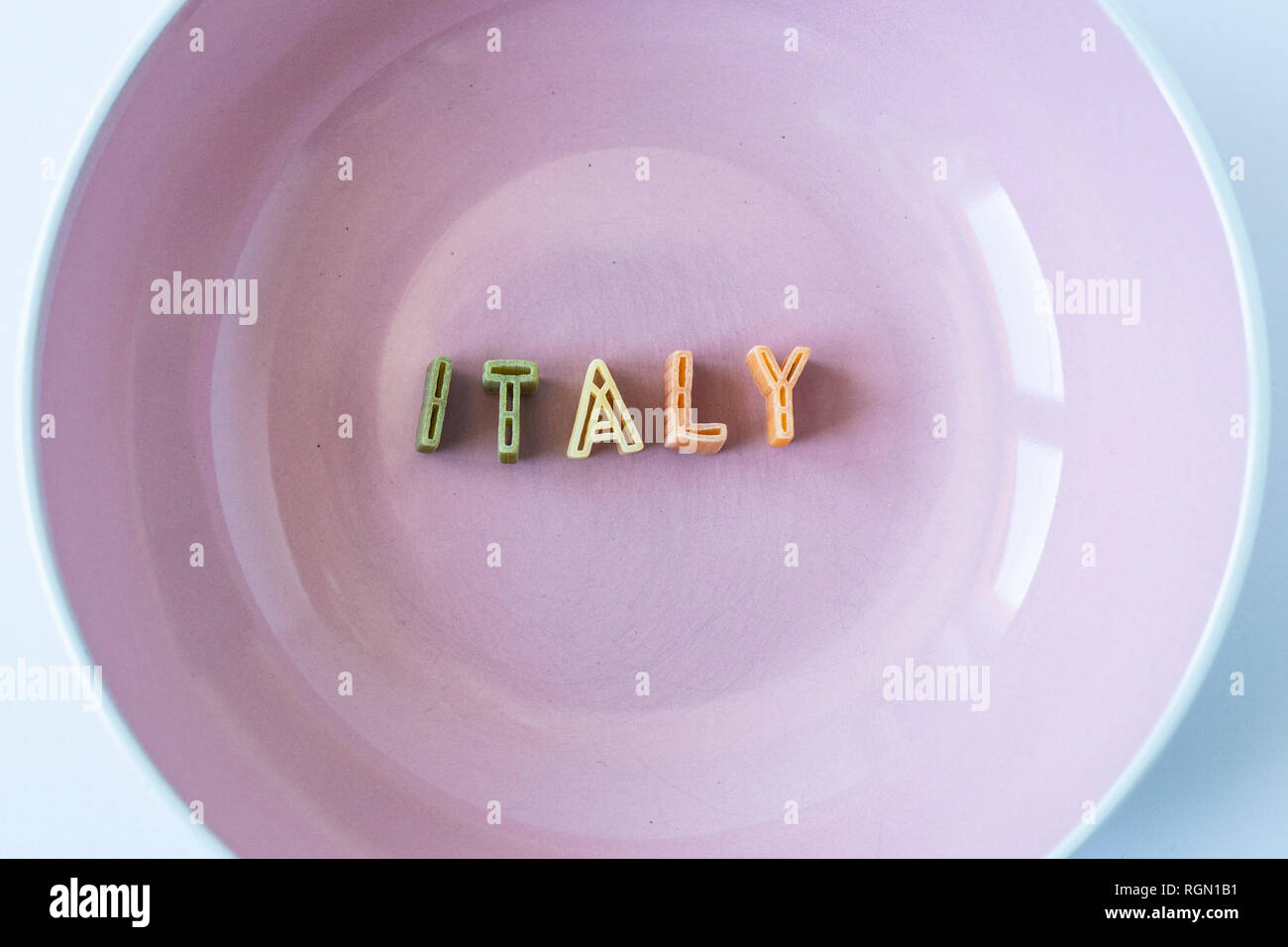 Le mot 'Italie' composé avec du vrai pâtes lettres dans le pavillon italien des couleurs dans un plat rose. Banque D'Images