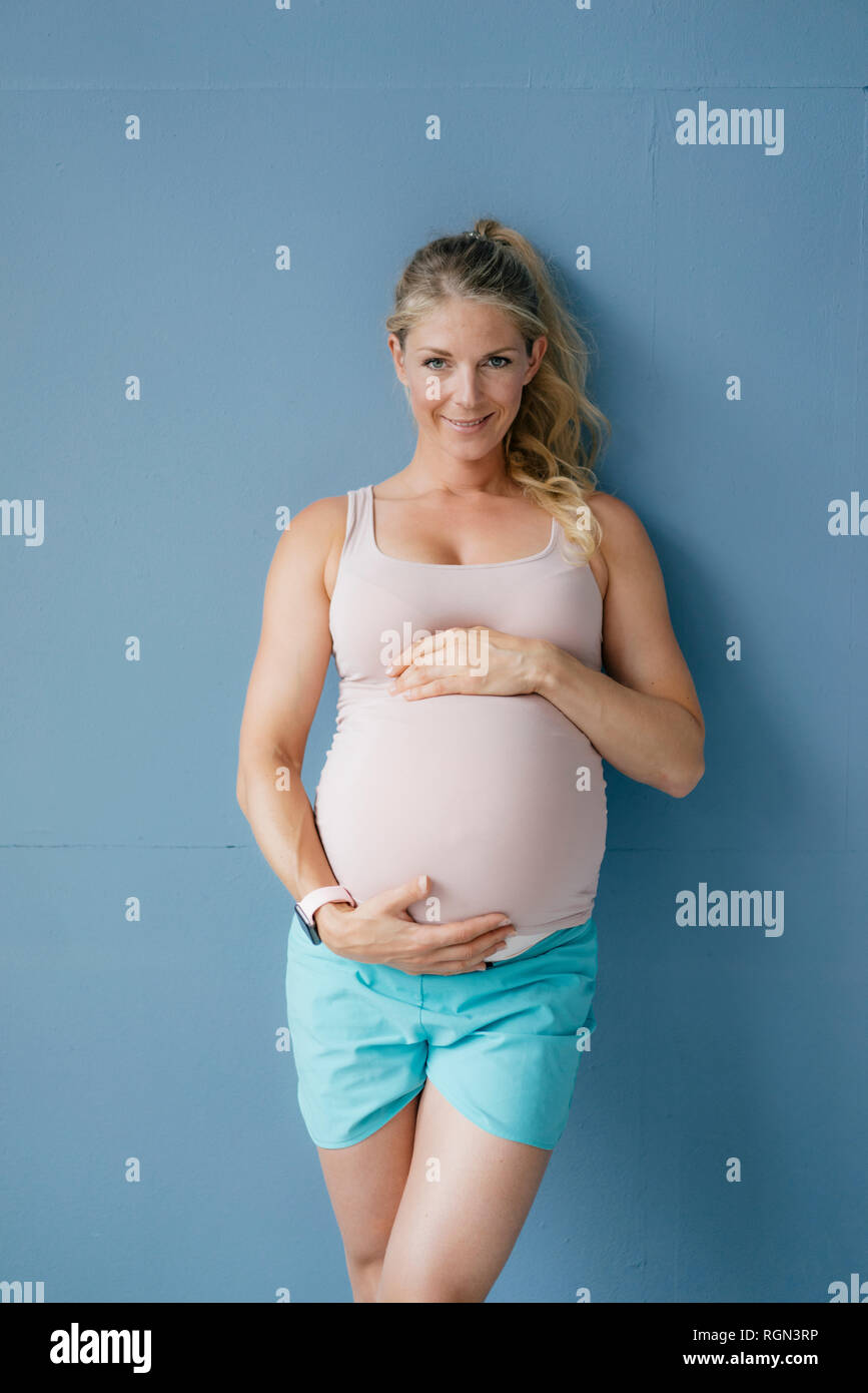 Portrait of smiling pregnant woman standing at mur bleu Banque D'Images