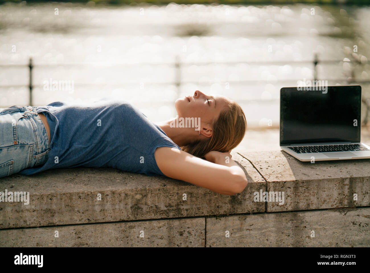 Jeune femme couchée sur un mur à côté d'un ordinateur portable Banque D'Images