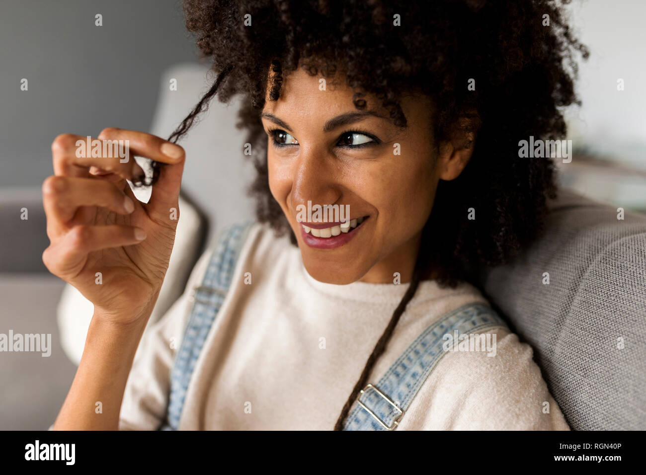 Portrait of smiling woman sitting on couch à examiner ses cheveux Banque D'Images