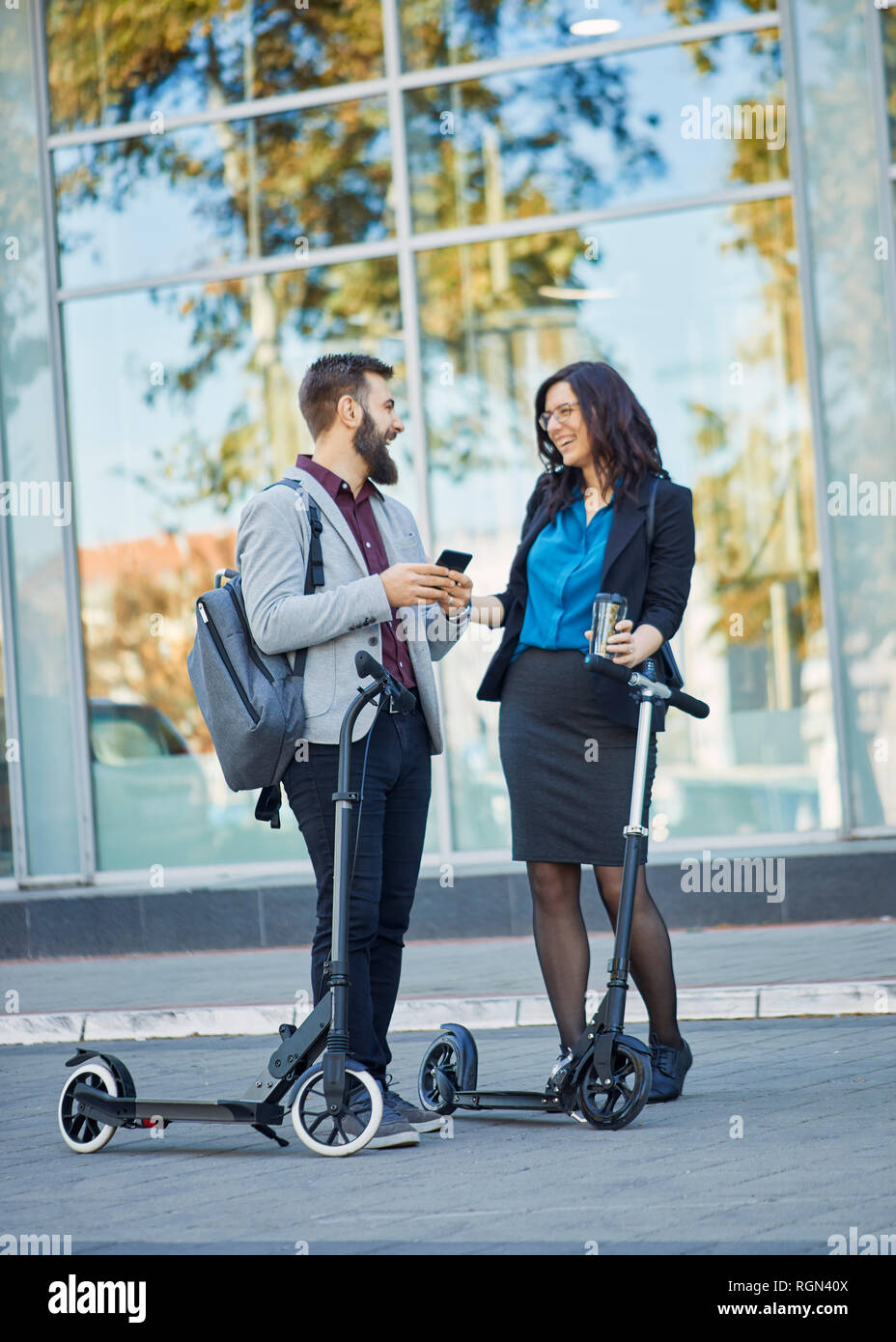 Happy businessman and businesswoman talking on scooters avec pavement Banque D'Images