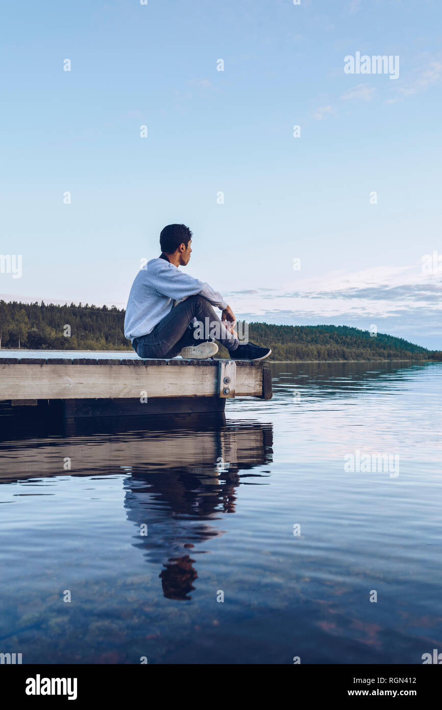 Jeune homme assis au bord du lac Inari, looking at view, Finlande Banque D'Images