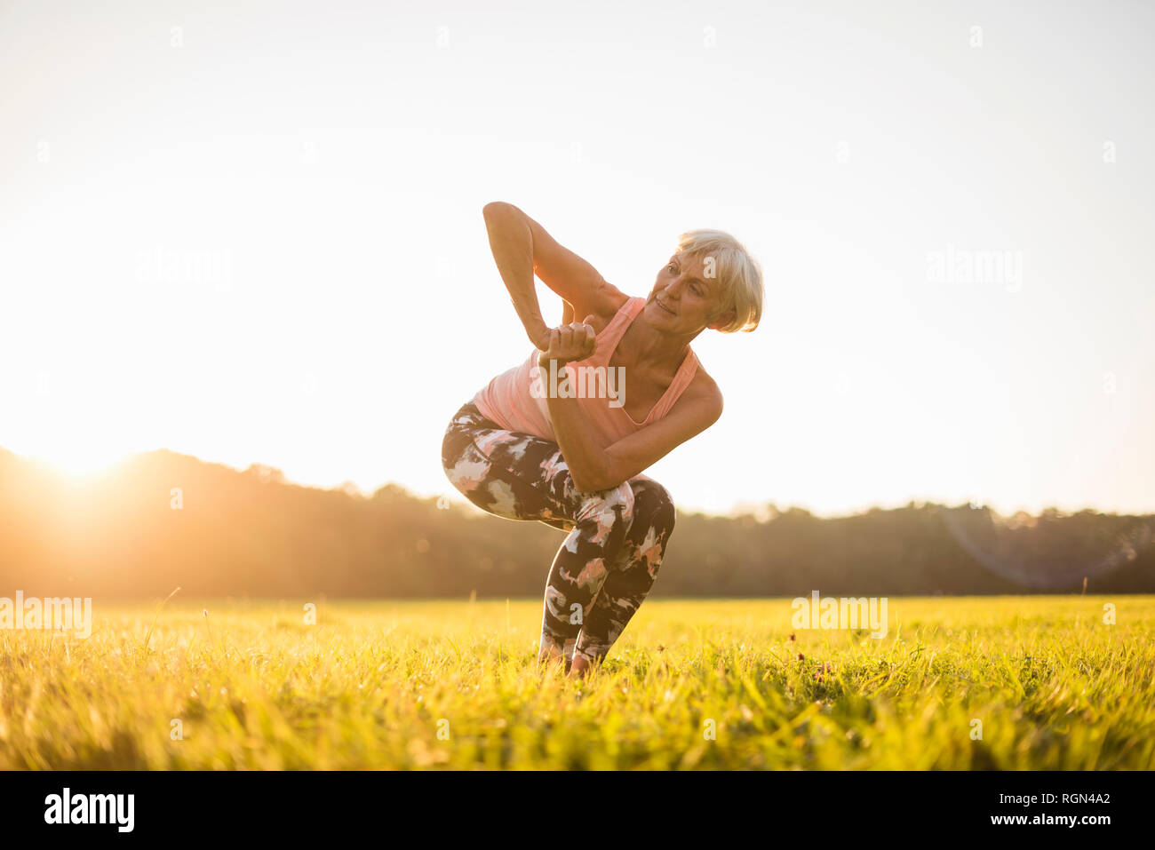 Senior woman doing yoga on rural meadow au coucher du soleil Banque D'Images