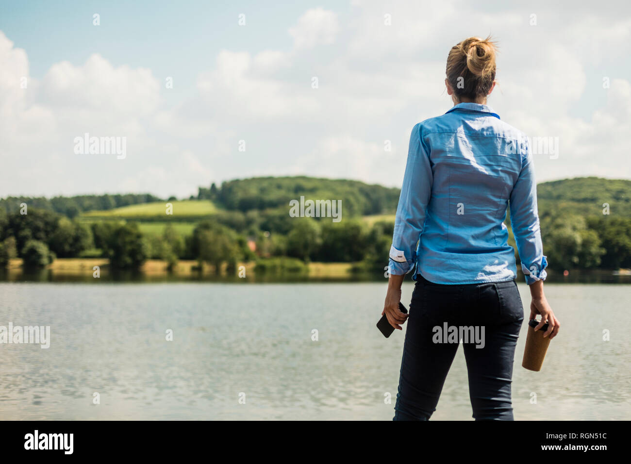 Femme debout dans un lac avec un téléphone cellulaire et du café à emporter Banque D'Images Femme debout dans un lac avec un téléphone cellulaire et du café à emporter Banque D'Images