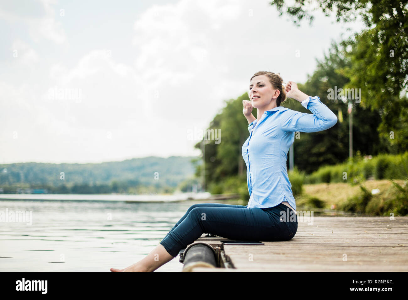 Woman sitting on jetty à un lac avec les pieds dans l'eau Banque D'Images