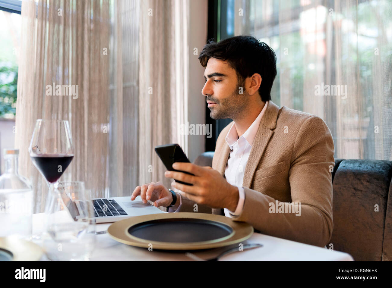 L'homme assis à table dans un restaurant à l'aide d'ordinateur portable et téléphone cellulaire Banque D'Images