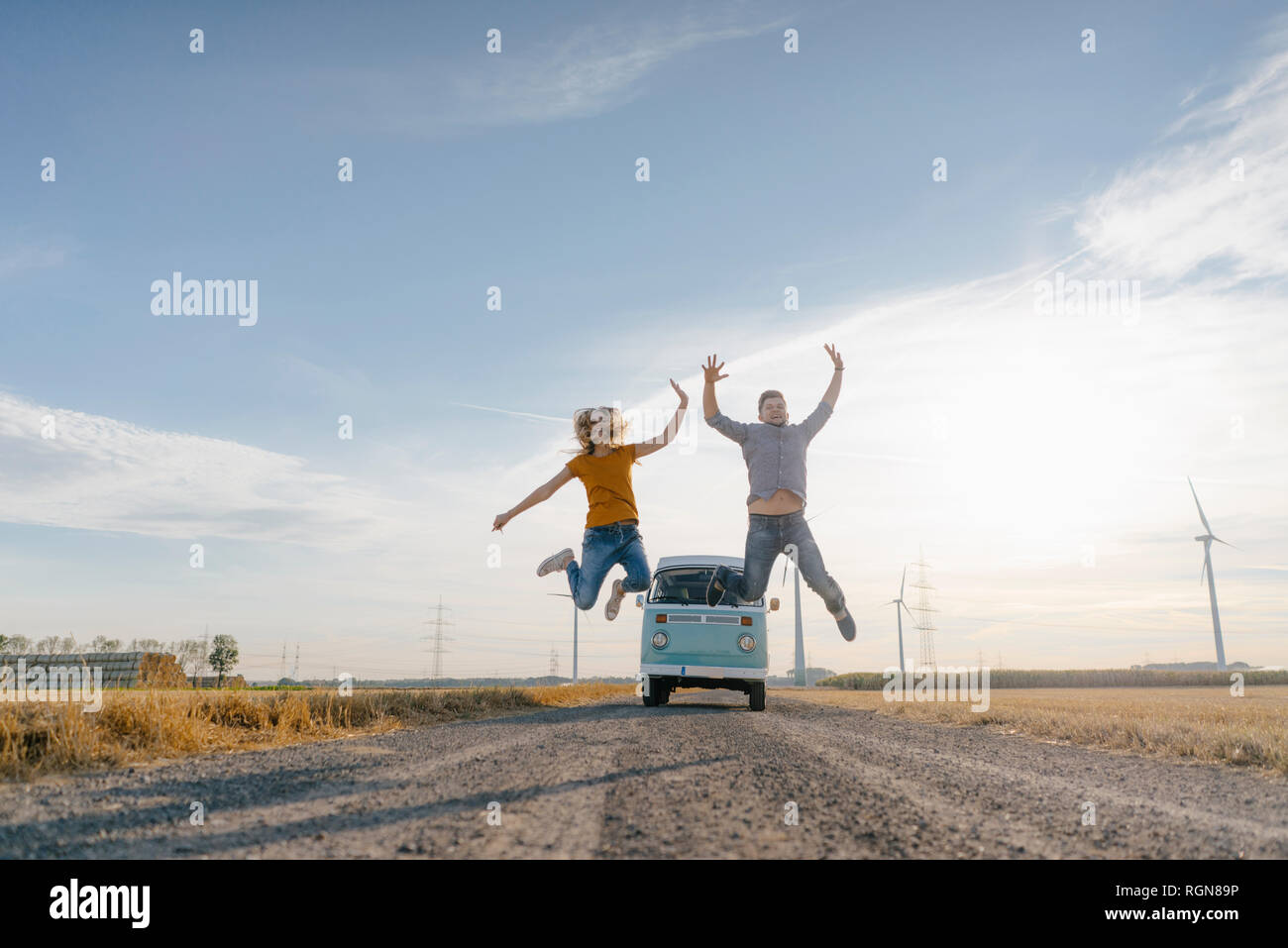 Couple exubérant de sauter sur un chemin de terre à camper van in rural landscape Banque D'Images