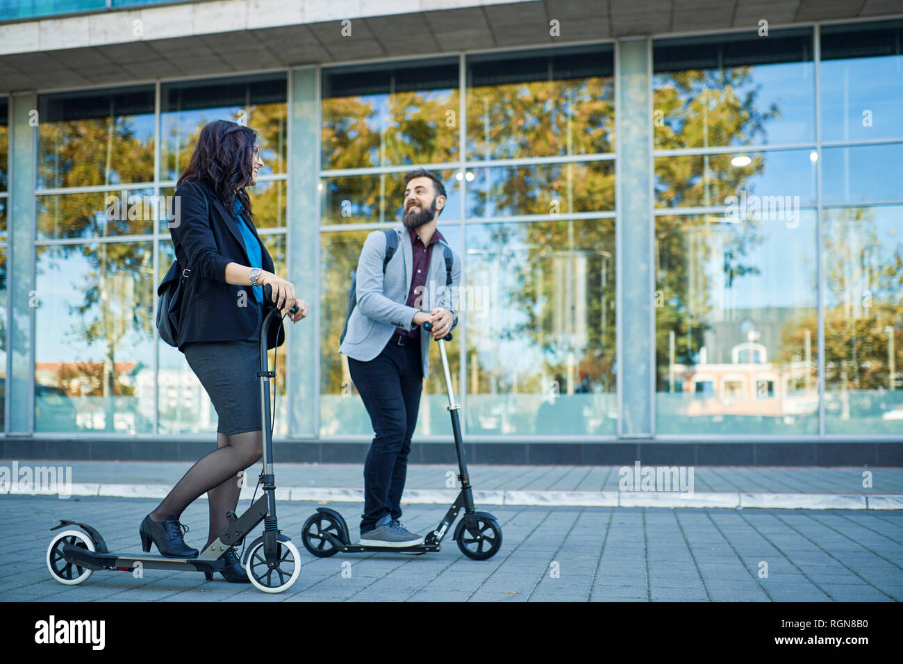 Smiling businessman and businesswoman talking on scooters avec pavement Banque D'Images