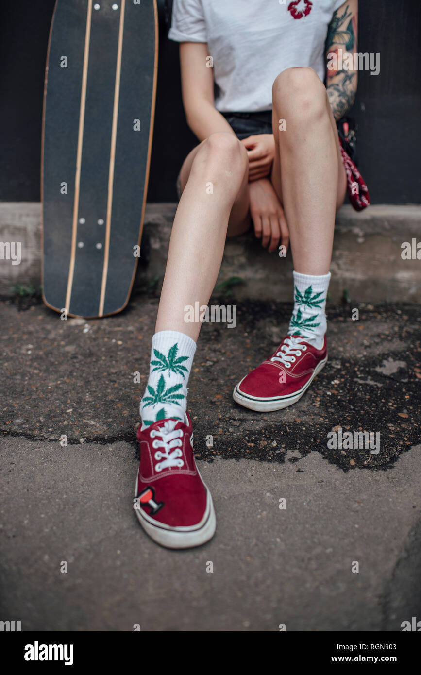 Les jambes de la femme dans les chaussettes et chaussures assis à côté de carver skateboard Banque D'Images