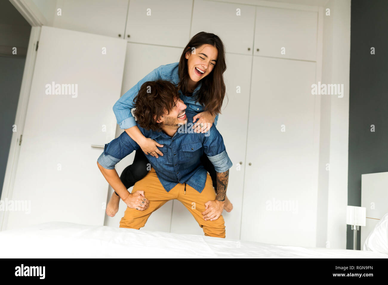 Cheerful man carrying girlfriend piggyback dans la chambre à la maison Banque D'Images