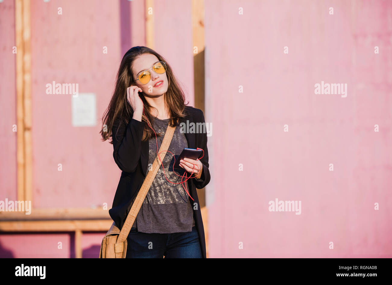 Young woman with cell phone et écouteurs portant des lunettes de couleur Banque D'Images