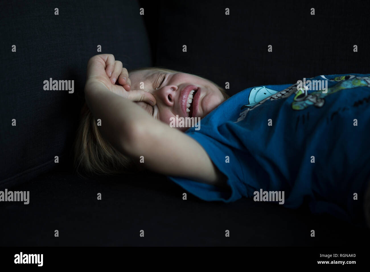 Crying boy lying on couch Banque D'Images