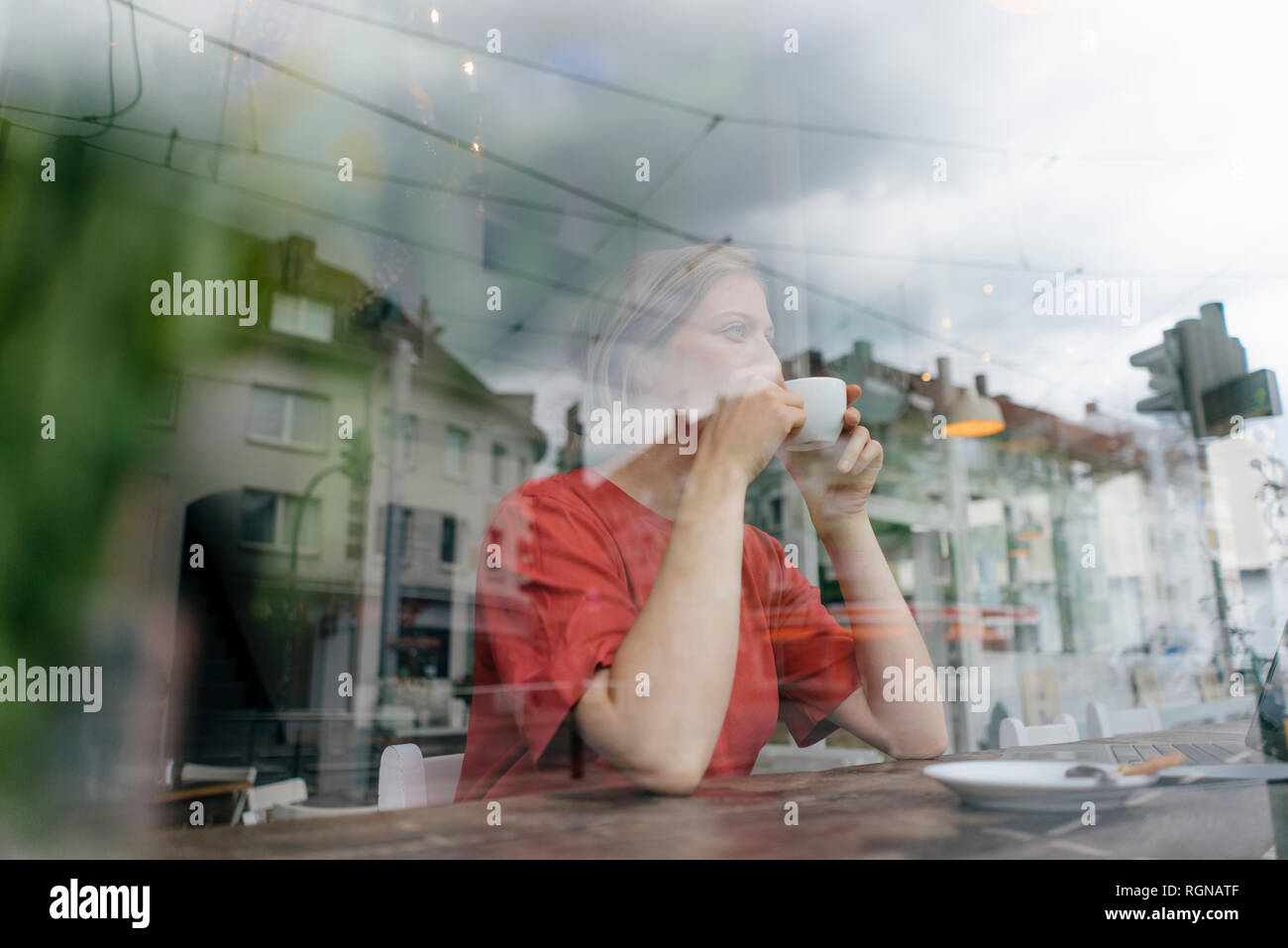 Jeune femme avec tasse de café derrière la vitre dans un café Banque D'Images