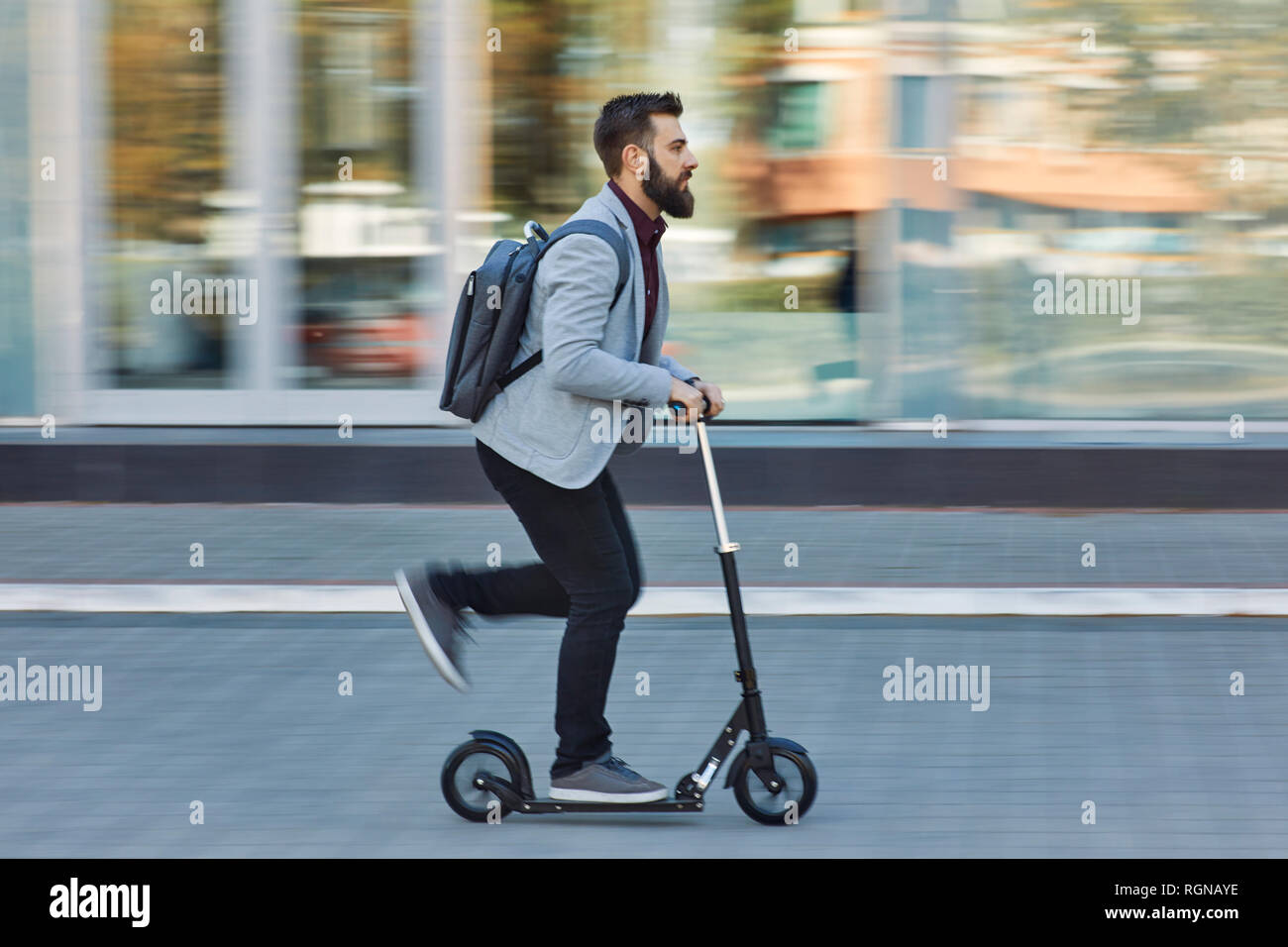 Businessman riding scooter le long office building Banque D'Images