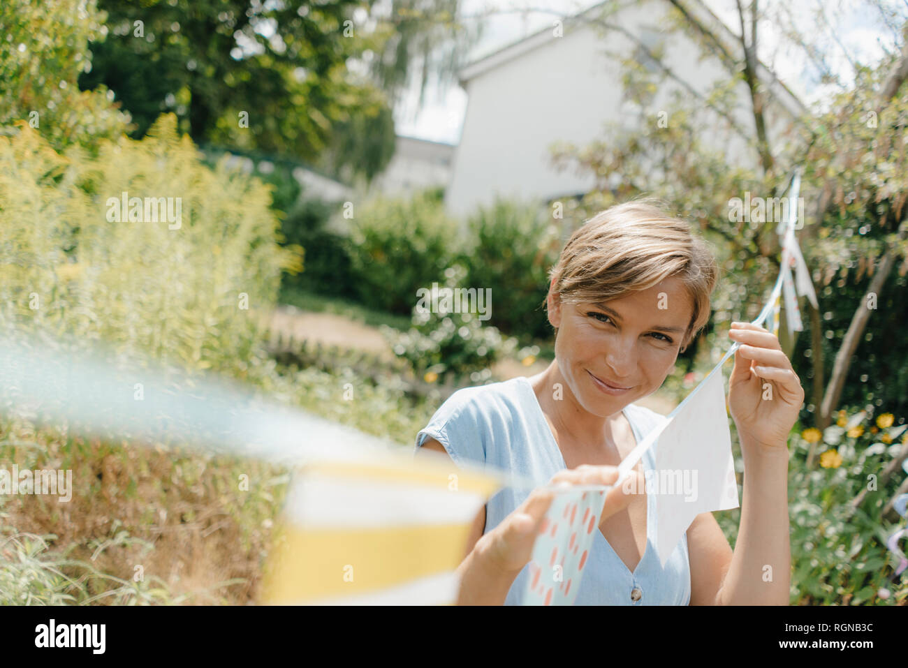 Portrait of smiling woman hanging up fanions dans jardin Banque D'Images