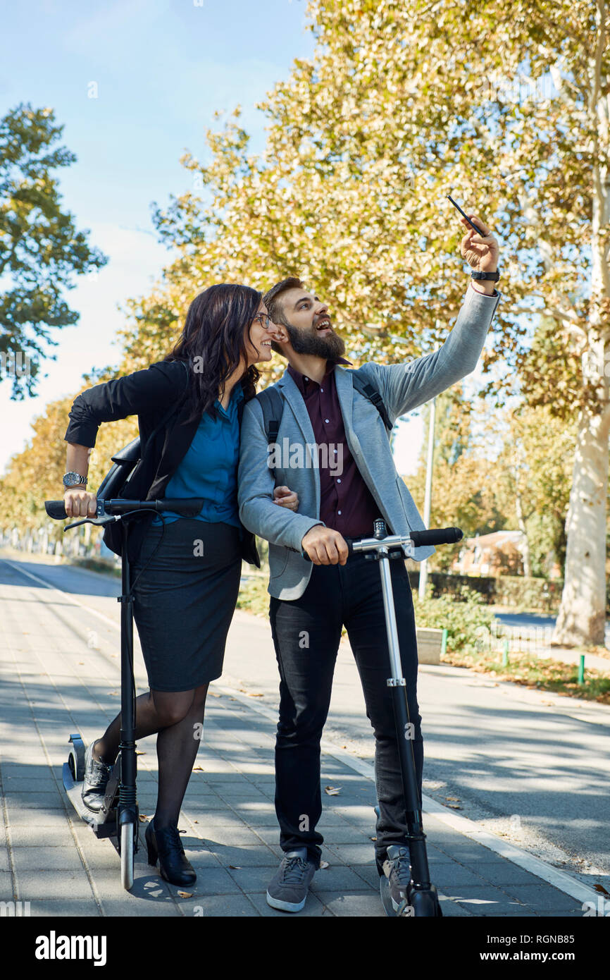 Happy business couple avec des scooters en tenant un selfies Banque D'Images