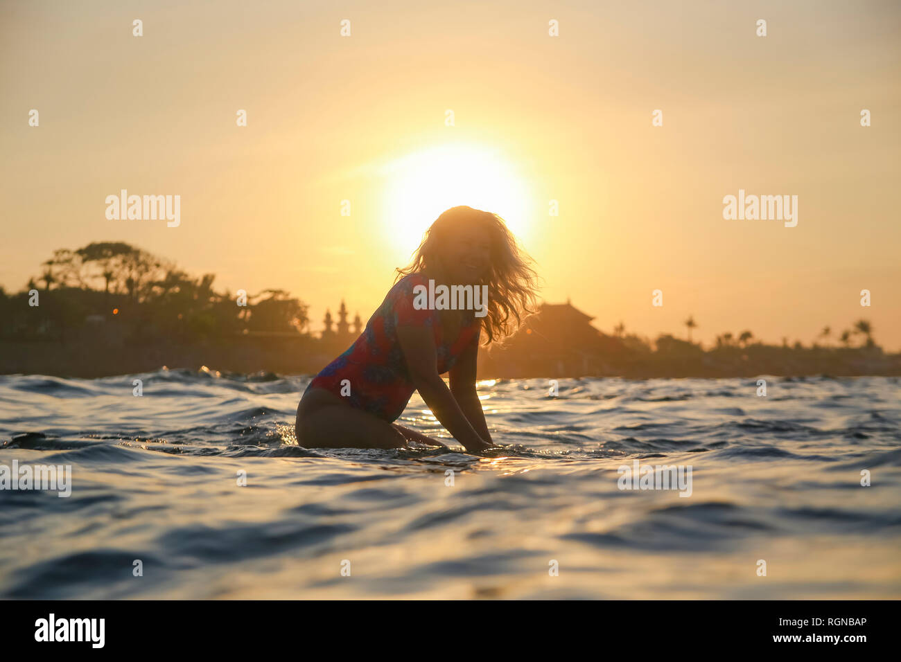 L'INDONÉSIE, Bali, pregnant woman sitting on surfboard au coucher du soleil Banque D'Images
