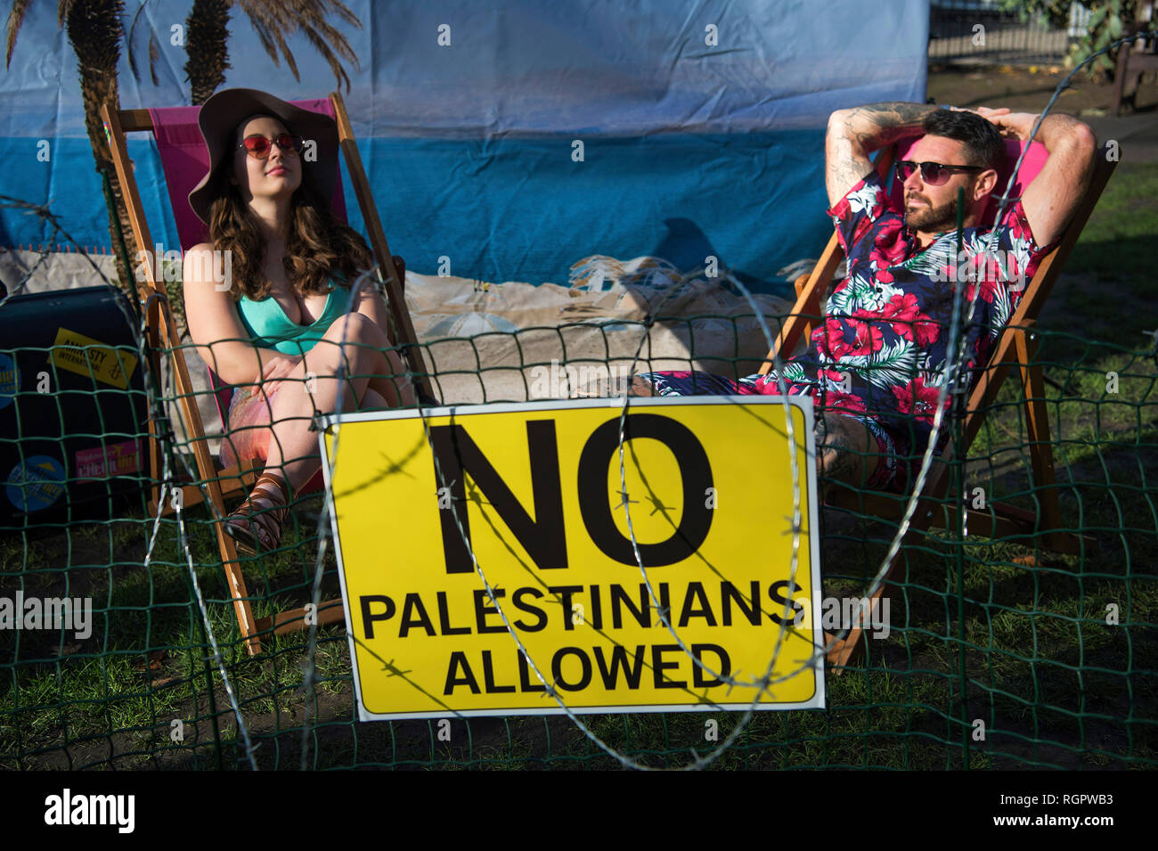 Deux modèles s'asseoir sur une plage "barbelés" devant les bureaux de TripAdvisor à Soho Square, centre de Londres, dans le cadre d'une campagne d'Amnesty International demande à l'entreprise et d'autres compagnies de voyage pour arrêter l'inscription chambres et activités dans les colonies de peuplement israéliennes dans les territoires palestiniens. Banque D'Images