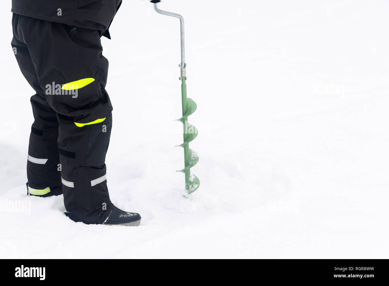 La pêche d'hiver sur la glace. L'homme de percer un trou dans la glace. Se détendre dans la nature Banque D'Images