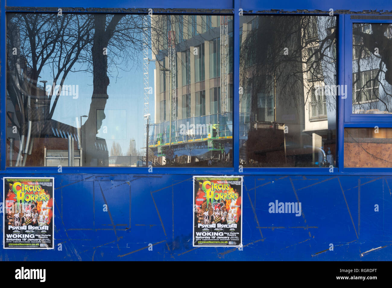 Reflet d'une tour en construction dans la fenêtre d'une boutique avec des affiches de cirque en ville Woking, Surrey, UK Banque D'Images