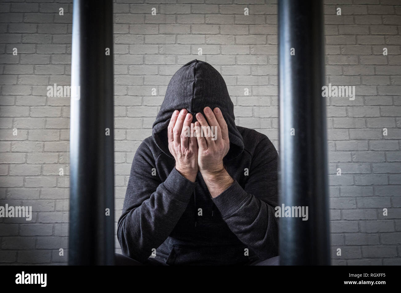 Un prisonnier avec sa tête dans ses mains derrière les barreaux dans une cellule de prison (photo posée par modèle) Banque D'Images
