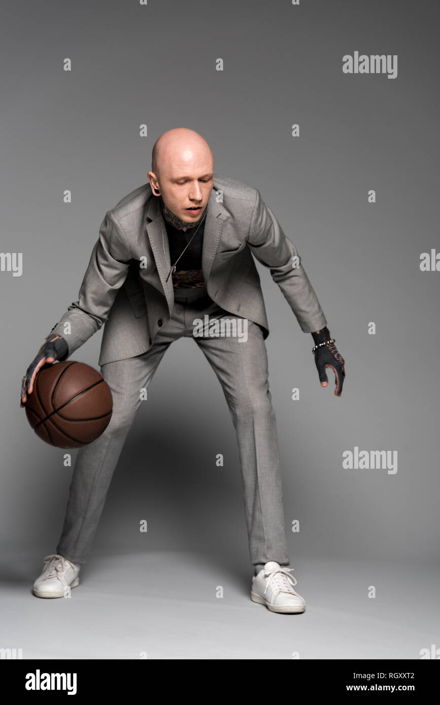 Sur toute la longueur de l'élégant tattooed man in suit jouer au basket-ball sur gris Banque D'Images