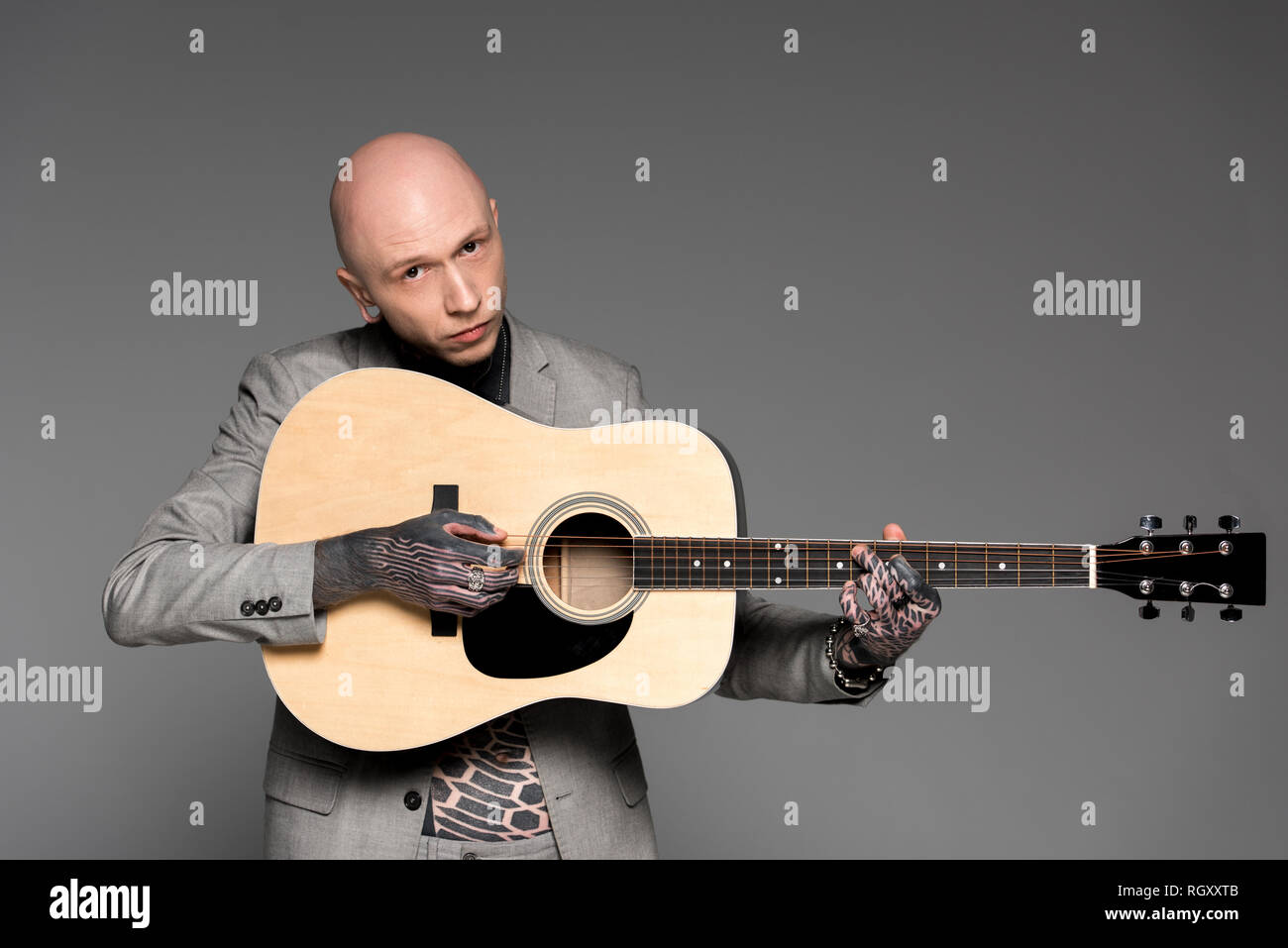 Handsome bald tattooed man in suit à jouer de la guitare et à la caméra à l'isolé sur gray Banque D'Images
