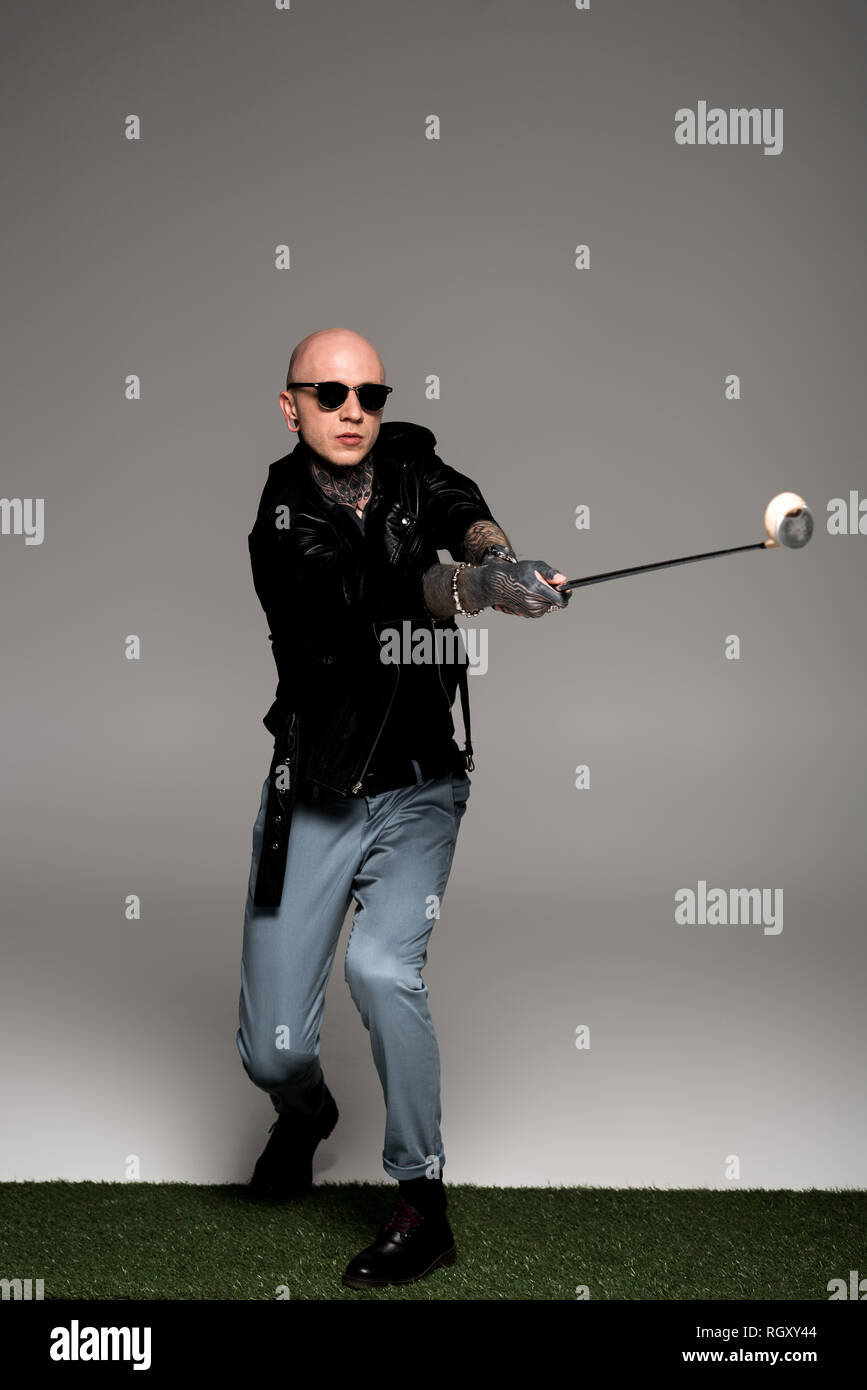 Tattooed man chauve en blouson de cuir et lunettes de soleil en jouant au golf sur gris Banque D'Images